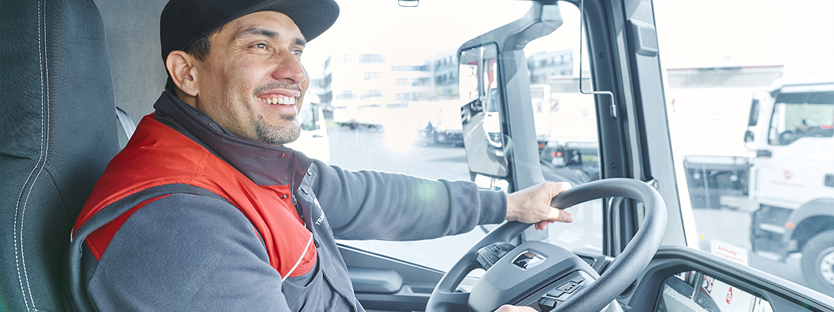 Eine Person in Arbeitskleidung steuert einen Lkw auf dem Gelände.