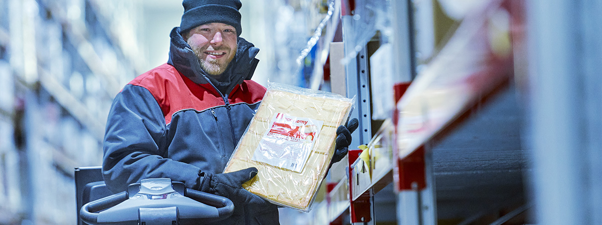 Eine Person steht in warmer Arbeitskleidung in einem Tiefkühllager und hält ein abgepacktes Lebensmittel in den Händen.