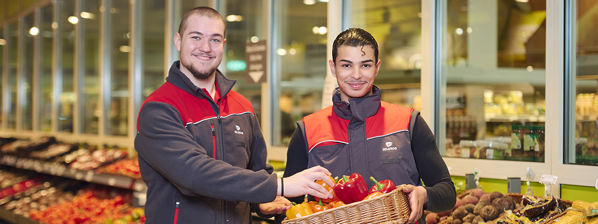 Zwei Personen in Arbeitskleidung präsentieren einen Korb mit frischem Gemüse in der Obst- und Gemüseabteilung einer Selgros-Filiale..
